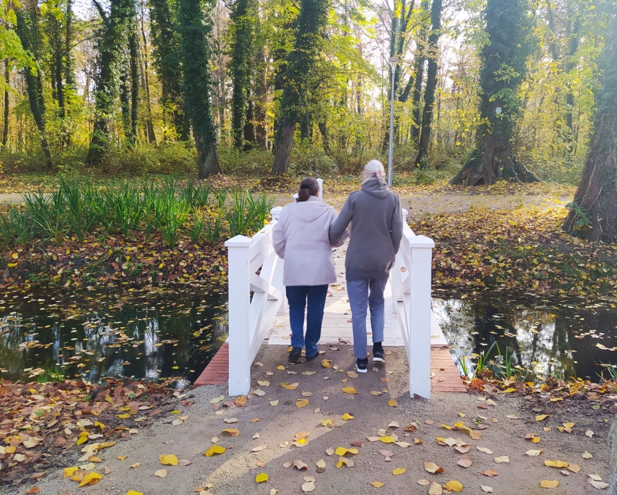 zdjęcie przedstawia seniorke ze swoją opiekunką na jesiennym spacerze w parku pałacowym w Zatoniu